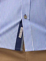 Camisa de manga larga con estampado de rayas verticales finas, cuello abotonado y cierre frontal con botones. Presenta un diseño clásico con detalle de logo bordado en el pecho.