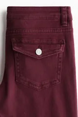 Pantalón de jean color bordó, de tiro bajo, corte ajustado hasta la rodilla y acampanado desde allí hacia abajo. Presenta cierre y botón frontal, bolsillos abiertos delanteros y bolsillos traseros con solapa y botón.