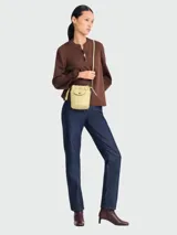 Bolso tipo crossbody de cuero en color amarillo pálido, con diseño de cubo, cierre de cordón ajustable y solapa con botón a presión.