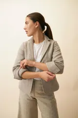 Chaqueta marrón de lana con cuello, solapa y bolsillos ojal. Forro solo en las mangas y terminaciones envivadas. Esquinas redondeadas y mangas con corte en puño que permiten transformarla en manga 3/4. Más larga en la espalda que en la delantera. Abrochadura con dos botones.