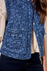 Chaleco capitoneado de jean azul con bordados florales en tono oscuro, cuello redondo y bolsillos delanteros aplicados con solapa fruncida.