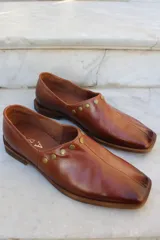 Zapato de cuero vacuno color bordó, con diseño de punta cuadrada y detalle de tachas metálicas planas en el borde superior. Presenta un taco geométrico bajo y costura central en el empeine.