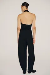 Body negro de cuello halter con escote drapeado pronunciado, detalle de flor blanca en relieve y espalda descubierta.