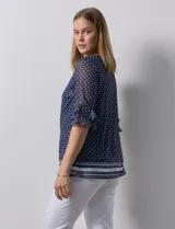 Blusa Harper de microtul estampado azul con lunares blancos, cuello redondo, escote en U con aplique de aros y mangas cortas amplias.