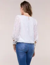 Blusa blanca de organza con textura devoré floral, silueta semiholgada y forro interno. Tiene escote bote, mangas largas abullonadas con transparencias, puños anchos con botones y ruedo elastizado.