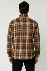 Sobrecamisa de franela a cuadros en tonos marrón, tostado, naranja y blanco, de manga larga con cierre frontal de botones y un bolsillo en el pecho.