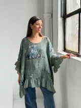Blusa verde de lino con estampado floral en tonos azules y grises, escote redondo, mangas 3/4 con volados y ruedo asimétrico con volado fruncido.