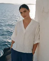 Blusa de lino color blanco, con cuello camisero y escote en V profundo, mangas 3/4 y corte holgado.
