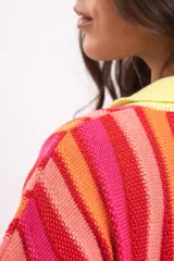 Vestido camisola corto de tejido fresco de algodón, con diseño a rayas verticales en tonos rojos, naranjas y fucsias. Cuenta con cuello polo y botonadura frontal en tono amarillo claro, y mangas cortas holgadas.