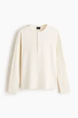 Remera de manga larga en tejido acanalado de algodón, color blanco, con cuello panadero redondo y tapeta corta con botones de ajuste. Corte slim fit que se ajusta a la silueta.