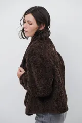 Chaqueta tipo gamulán de color marrón, con solapas amplias forradas en corderito sintético oscuro. Presenta un diseño cruzado con botones frontales y mangas largas, ideal para un estilo invernal.