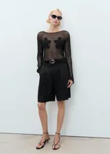 Jersey de punto grueso negro con cuello barco, manga larga y detalles florales bordados en el frente.