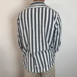 Camisa de lino de corte oversize con diseño de rayas verticales en tonos blanco y tostado, manga larga y cierre frontal con botones.