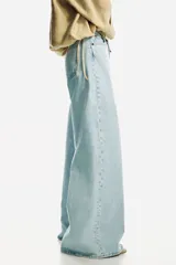 Jean de denim de algodón rígido, de color celeste claro, con tiro alto y pierna amplia de corte extraholgado. Presenta diseño clásico de cinco bolsillos, cierre frontal con cremallera y botón metálico.