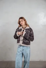 Campera de gamuza con estampado animal print en tonos grises, forrada con corderito sintético en color crema. Presenta cierre frontal con botones tipo toggle y detalles de costuras visibles.