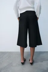Bermuda de tiro medio color negro con bolsillos en el delantero y detalle de pinzas. Cuenta con cierre frontal con cremallera y ganchos metálicos.