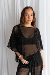 Blusa de tul negro semitransparente con diseño de mangas murciélago amplias y aplicación de pequeños puntos brillantes plateados distribuidos por toda la prenda.