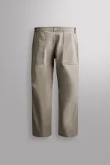 Pantalón de corte tapered fit color beige, confeccionado en tejido ligero de algodón con estructura rip stop. Cuenta con bolsillos de plastrón delanteros con acceso curvado, pinzas en las rodillas para mayor movilidad, y cierre frontal con cremallera y botón a presión.