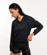 Campera rompevientos deportiva negra, confeccionada en poliamida, con capucha, cierre delantero en cremallera, tirador gomoso, puños ajustados y detalles de malla en los laterales.