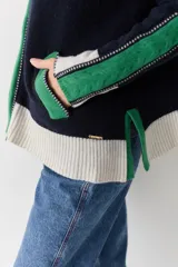 Campera de lana con cierre frontal de doble cursor y cuello alto. Presenta un diseño en bloques de color azul marino, verde y crema, con detalles de tejido trenzado en las mangas y bolsillos laterales con contraste.