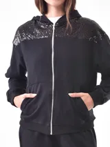 Campera deportiva negra con capucha, cierre frontal y apliques de lentejuelas en los hombros.