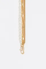 Collar de estilo multicadena con múltiples tiras entrelazadas: una de perlas pequeñas, dos de cadena dorada con pequeñas incrustaciones de esmalte de colores, y una de cadena dorada lisa. Finaliza con un dije circular dorado con forma de corazón calado en el centro.