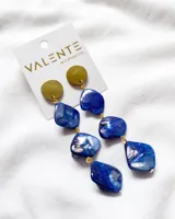 Aros colgantes con base circular dorada y piedras nacaradas azules de diferentes formas unidas por argollas doradas.
