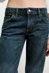 Jeans de mezclilla azul oscuro con efecto lavado, tiro bajo y pierna ancha extra larga. Modelo de cinco bolsillos con cierre frontal de cremallera y botón metálico.