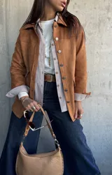 Chaqueta de gamuza color camel, con corte recto, cuello camisero, cierre frontal con botones metálicos y bolsillos frontales con solapa.