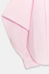 Camisa de algodón de corte oversize, color rosa claro, con cuello solapa, manga larga con puños y cierre frontal con botones. Presenta detalles de pliegues en el delantero.
