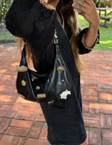 Cartera tipo baguette de gamuza color chocolate, con diseño decorado con diversos apliques metálicos, perlas y piezas de piedra. Cuenta con cierre superior y correa ajustable.