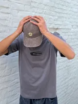 Gorro estilo jockey de color gris oscuro con efecto desgastado y un logo circular bordado en color beige claro en el frente.