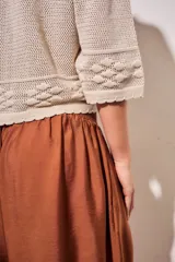 Cardigan de algodón peinado color beige, con cuello camisero, cierre frontal de botones y detalles de textura en crochet con diseño de flores. Mangas tres cuartos y diseño corto.