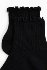 Medias tobilleras negras de punto acanalado con borde superior elástico fruncido.