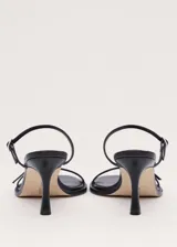 Sandalias de tacón alto color negro, con diseño minimalista de tiras finas cruzadas en el empeine y cierre con hebilla en el tobillo.
