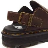 Muecas o zapatos destalonados Dr. Martens modelo Zebzag de cuero marrón, con tira ajustable con hebilla metálica y suela chunky acanalada con costura amarilla característica de la marca.