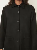 Sobrecamisa negra de corte recto y largo medio, con cuello clásico, cierre frontal de botones y dos bolsillos frontales aplicados.