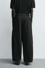 Pantalón de corte balloon fit y estilo relajado, confeccionado en tejido de algodón. Presenta pliegues frontales, cintura con trabillas, cierre frontal con cremallera y botón, bolsillos delanteros y bolsillos traseros de vivo.