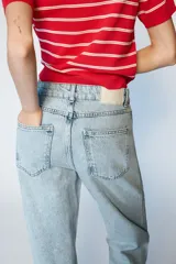 Jeans de tiro alto con diseño de cintura cruzada, cinco bolsillos y pernera recta con bajo sin costura. Cierre frontal con cremallera y botones.