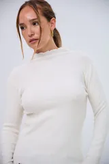 Polerita de manga larga color crudo, de tejido acanalado, con cuello alto y bordes ondulados.