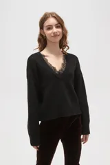 Sweater negro de punto con escote en V profundo y detalle de encaje en el borde del cuello. Presenta mangas largas con puños acanalados y un corte holgado.