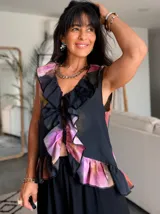 Musculosa negra con estampado floral en tonos rosa, naranja y marrón, con volados en el escote y ruedo. Cierre frontal con botones.