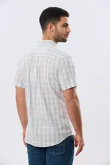 Camisa de manga corta confeccionada en mezcla de lino y algodón, con diseño a cuadros en tonos gris, blanco y azul. Presenta cuello camisero con botones y bolsillo ojal en el pecho con detalle bordado.