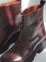 Botas de cuero color marrón con suela track negra y cierre frontal con cremallera roja.