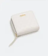 Billetera pequeña color blanco con textura geométrica de triángulos. Tiene cierre perimetral con cremallera, monedero interno con cierre, múltiples ranuras para tarjetas y logo metálico dorado en la esquina inferior.
