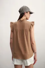 Camisa color amarillo pálido con textura arrugada, cuello mao con volados, cierre frontal con botones y mangas cortas con volados.