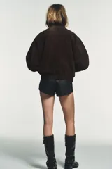 Cazadora tipo bomber de Zara confeccionada en piel de ante 100%. Presenta cuello redondo, cierre frontal con cremallera metálica, bolsillos delanteros con solapa y bajo con acabado elástico.