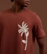 Remera marrón de corte regular, cuello redondo y manga corta, con estampa bordada de una palmera en el frente.