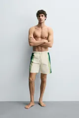 Bañador de hombre color blanco con diseño de bandas verticales en tonos de verde, simulando un efecto tie-dye o acuarela. Posee cintura ajustable con cordón, bolsillos laterales y forro interior.