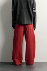 Pantalón wide fit color rojo terracota, con pliegues frontales, bolsillos laterales y cierre frontal con cremallera y botón.